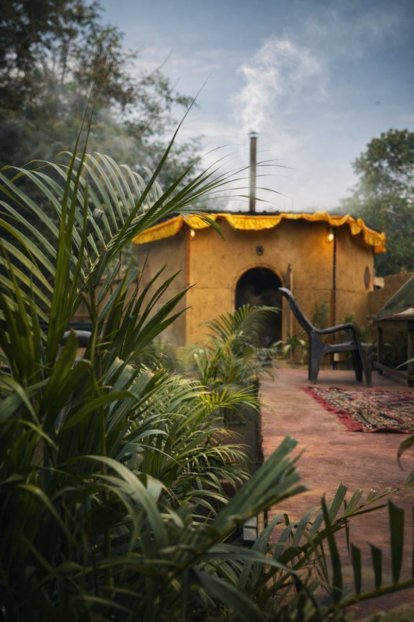 Hidden Oak mud-and-wood banya at golden hour among palms